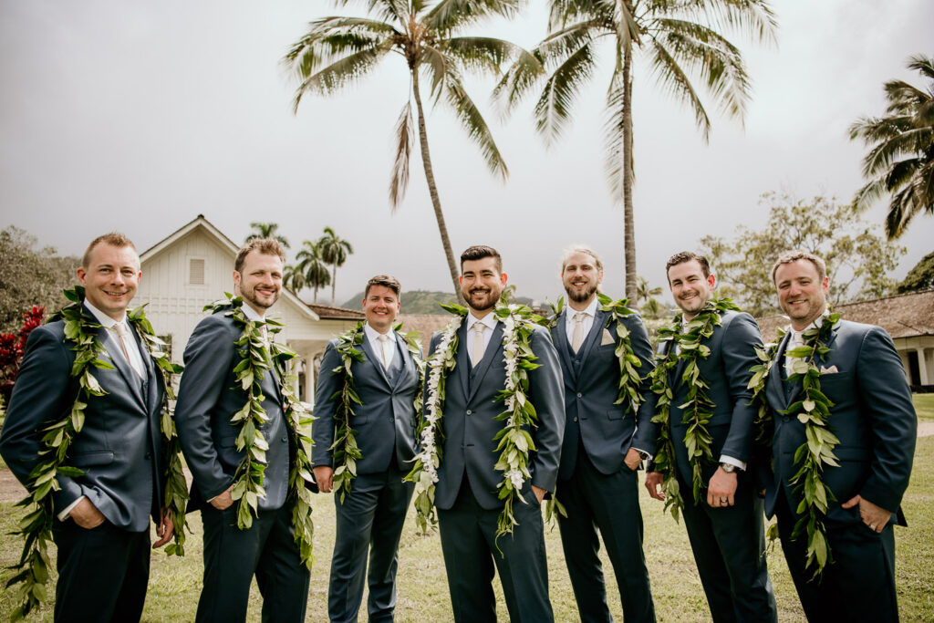 Groom and six groomsmen in blue suits with palm trees in background.