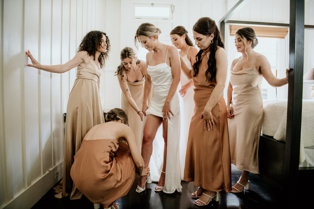Bridesmaid helping bride put on her shoes.