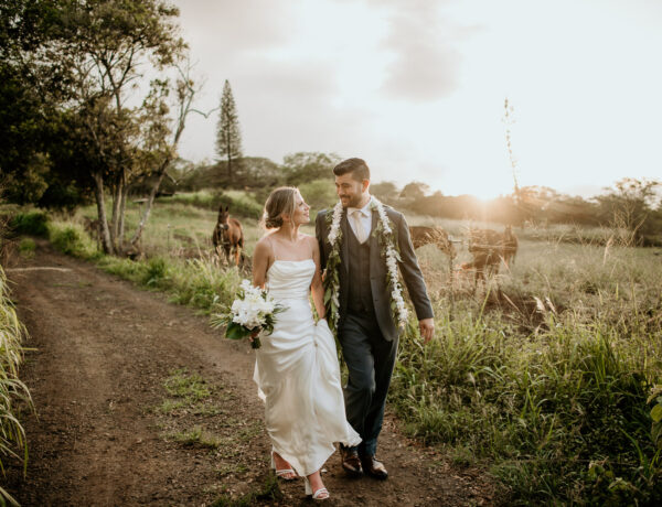 Bride and Groom walking along dirt pathway at Dillingham Ranch with horses in the background at sunset.