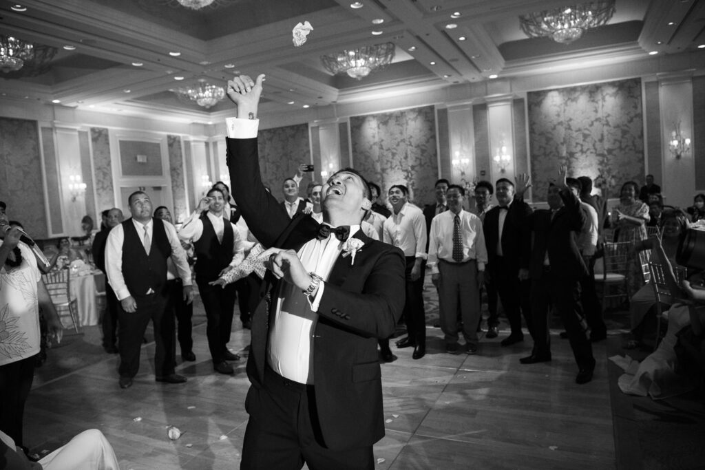 Black and White image of Groom tossing garter to single men at the wedding reception in the Ocean Ballroom Four Seasons Koolina.