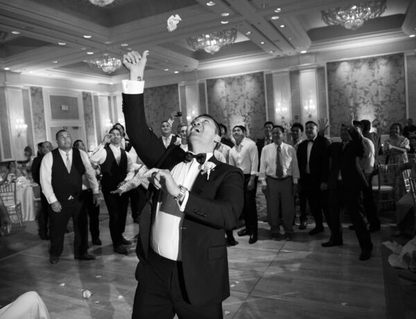 Black and White image of Groom tossing garter to single men at the wedding reception in the Ocean Ballroom Four Seasons Koolina.