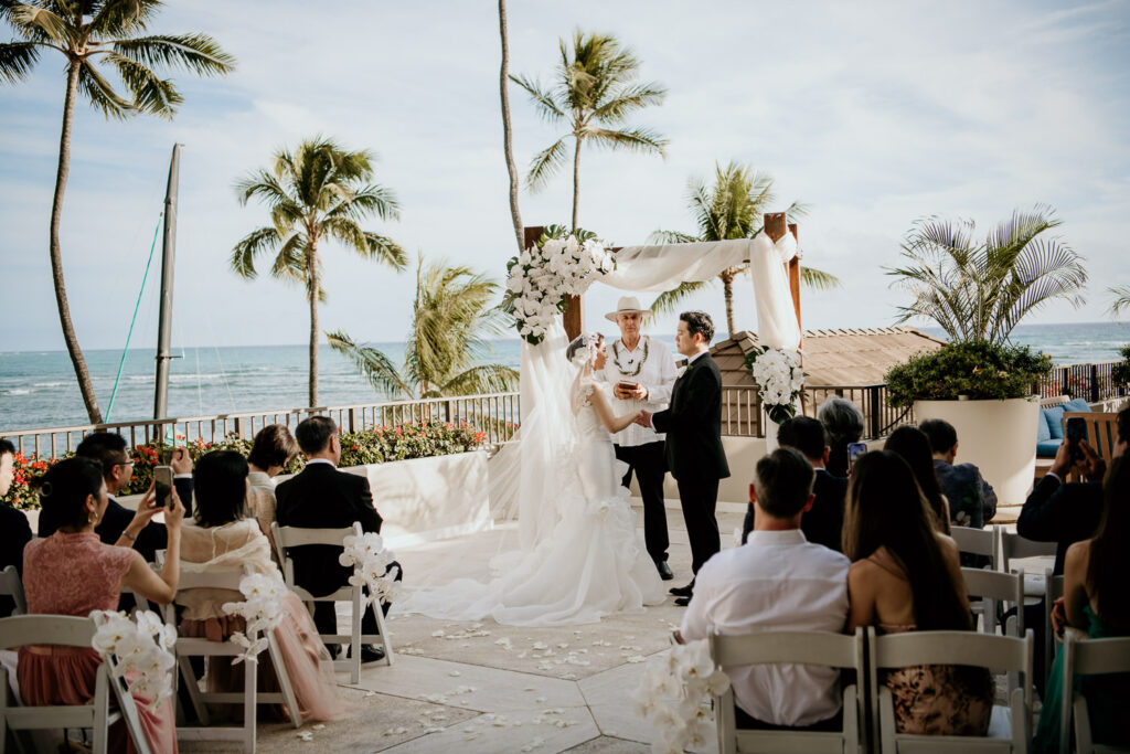 Wedding Ceremony at the Halekulani Hau Terrace with Waikiki Beach and Palm trees in the background.