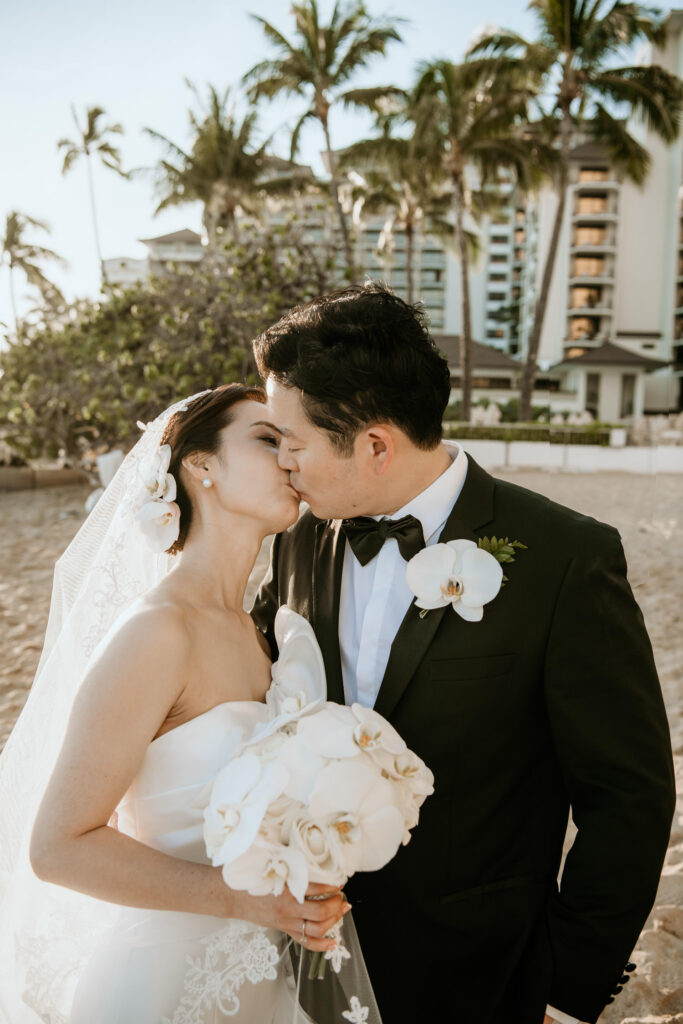 Groom kissing Bride with Halekulani in Background on Waikiki beach.