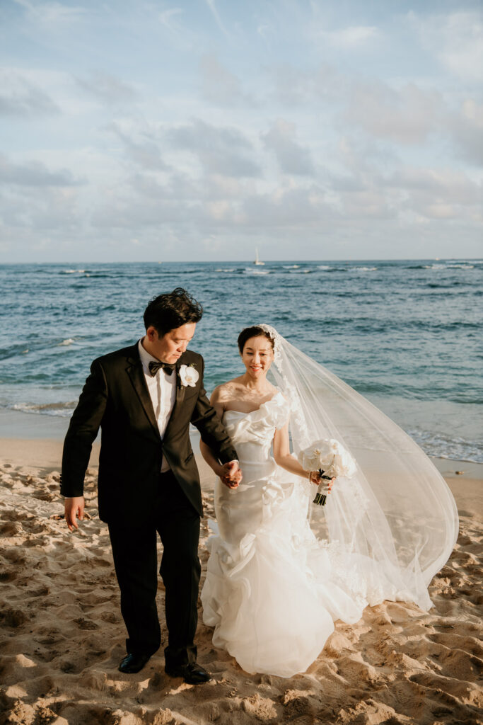 Bride and Groom walking on the beach in front of Halekulani Hotel.