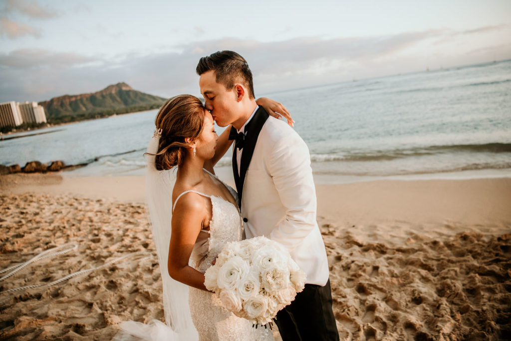Groom kissing bride on forehead in front of Diamond Head