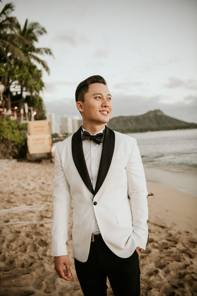 Groom in white tux with black lapel and black bowtie on beach