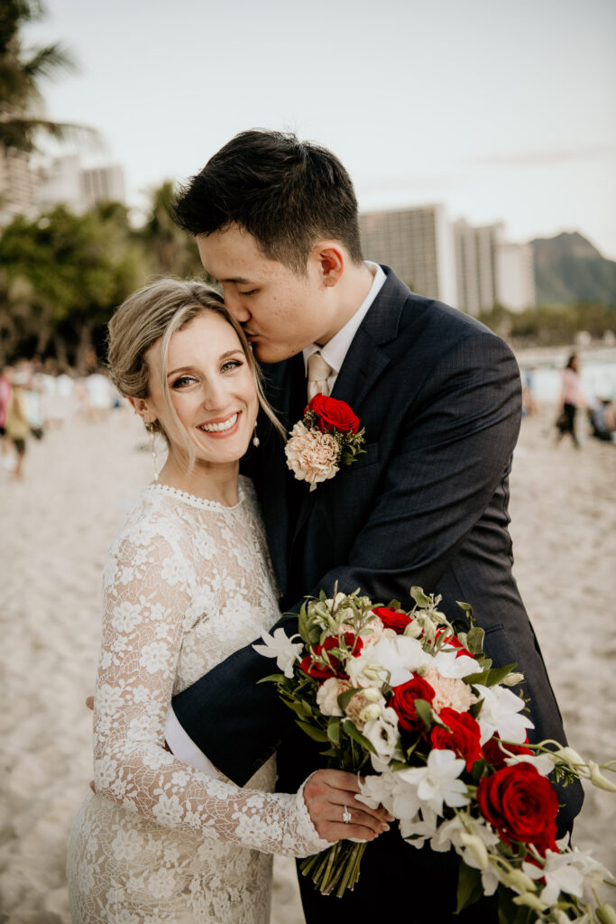 Groom embracing bride on Waikiki Beach.